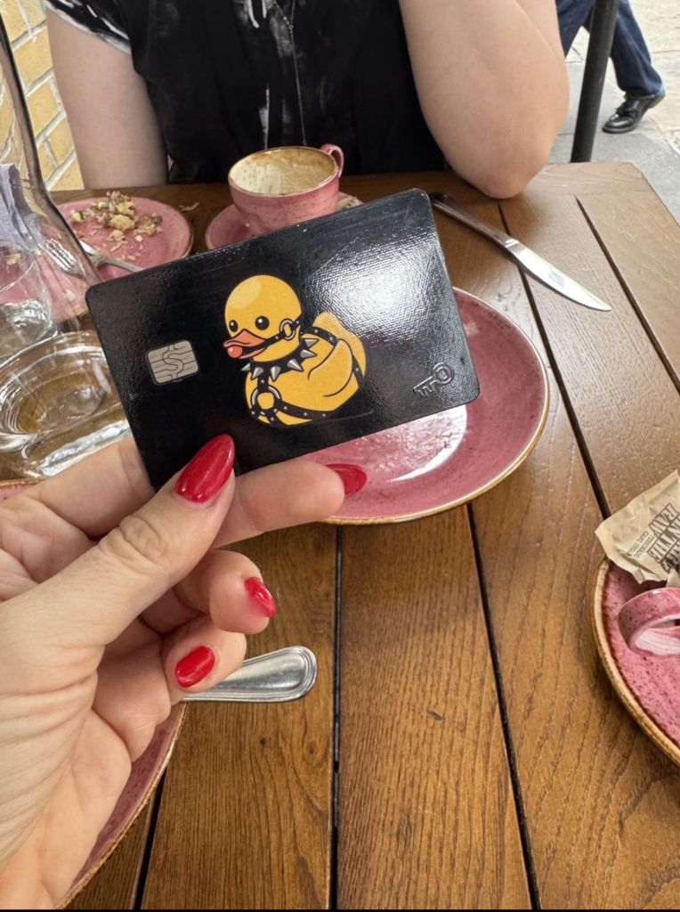 mistress blunt holds a credit card with a yellow duck on it as she pays for a meal on a date with her submissive's credit card